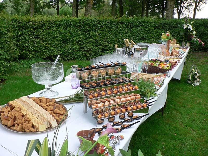 Table de buffet en extérieur avec verrines, amuse-bouches, pains, boissons et décorations végétales.