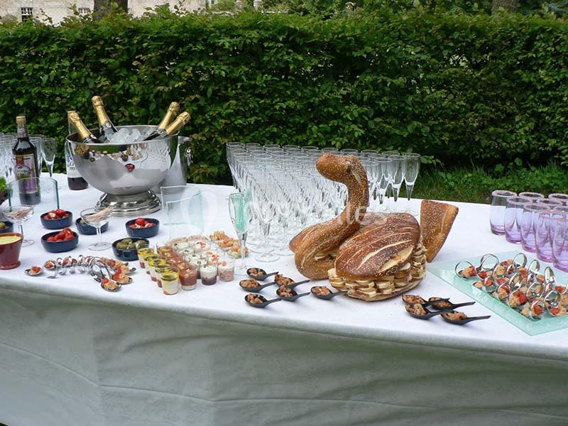 Table dressée avec des coupes de champagne, amuse-bouches variés et pain en forme de cygne, en extérieur.