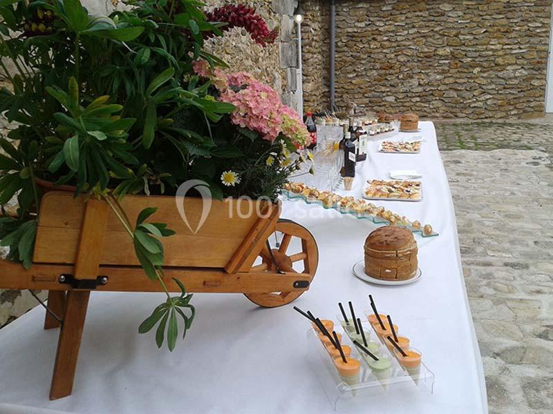 Table de buffet en extérieur avec des plats variés, une charrette en bois décorative et des fleurs en arrière-plan.