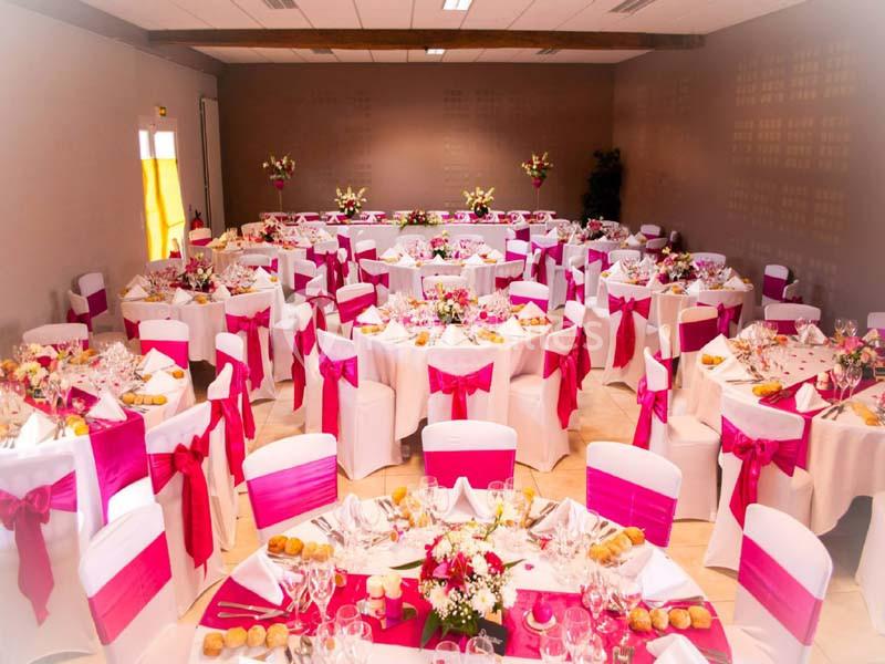 Salle de réception décorée avec des nappes blanches et des nœuds roses, tables dressées pour un événement festif.