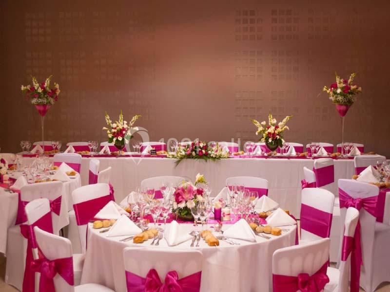 Salle de réception décorée avec des nappes blanches, des rubans roses et des compositions florales sur les tables.
