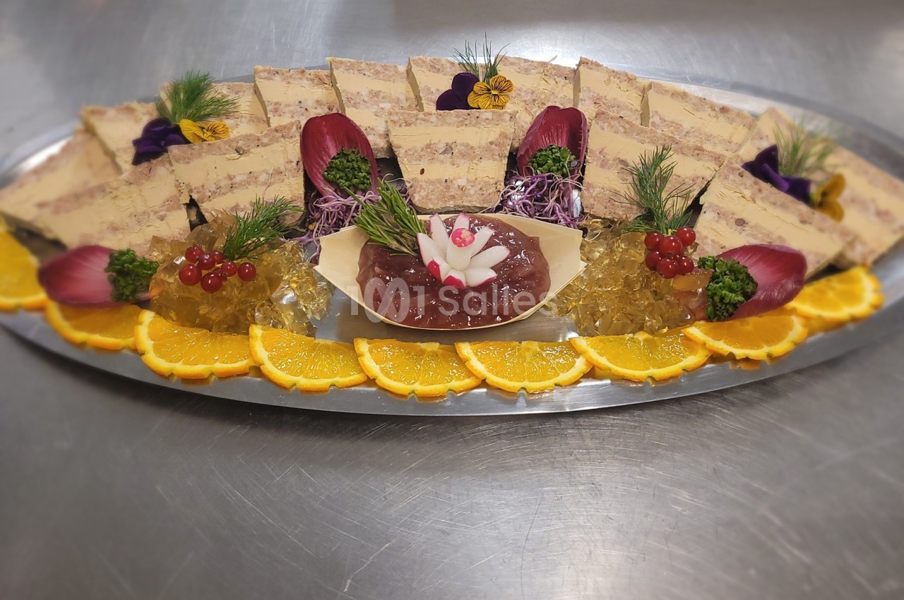 Plateau de terrines garnies de gelée, tranches d'orange, groseilles et décorations florales sur une table en inox.