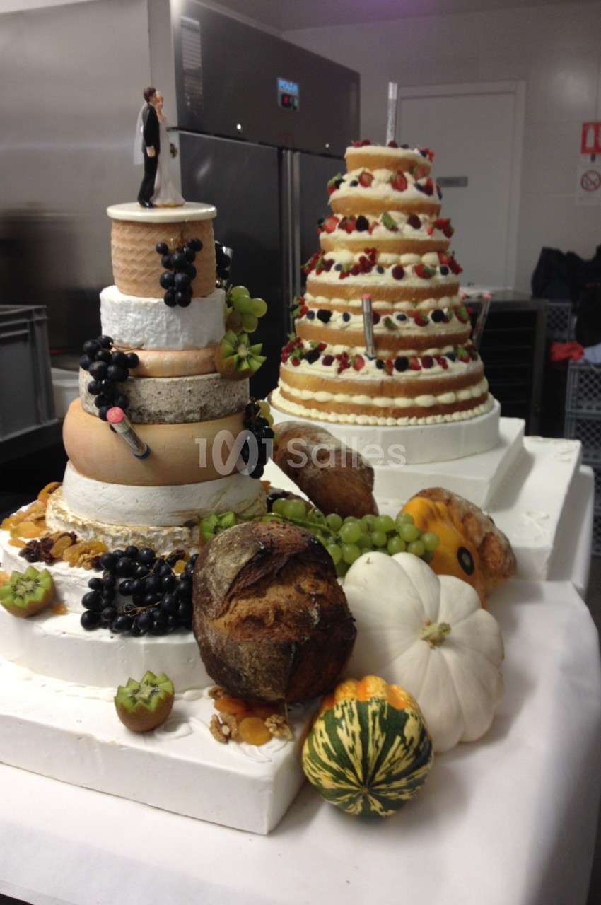 Plateau de fromages en pyramide accompagné de fruits, pains et courges décoratives dans une cuisine professionnelle.