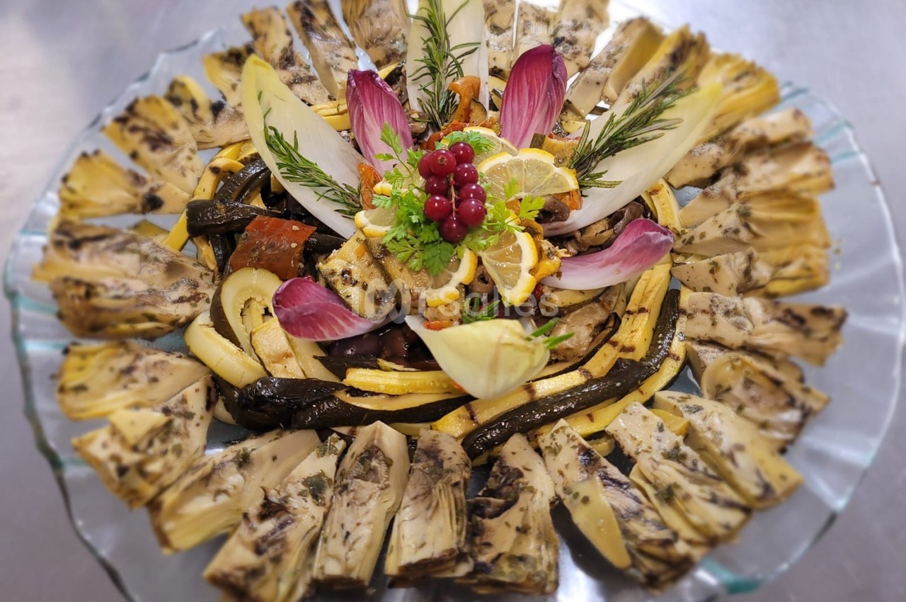Plateau de légumes grillés et marinés disposés en cercle avec des garnitures de feuilles, herbes et fruits rouges.