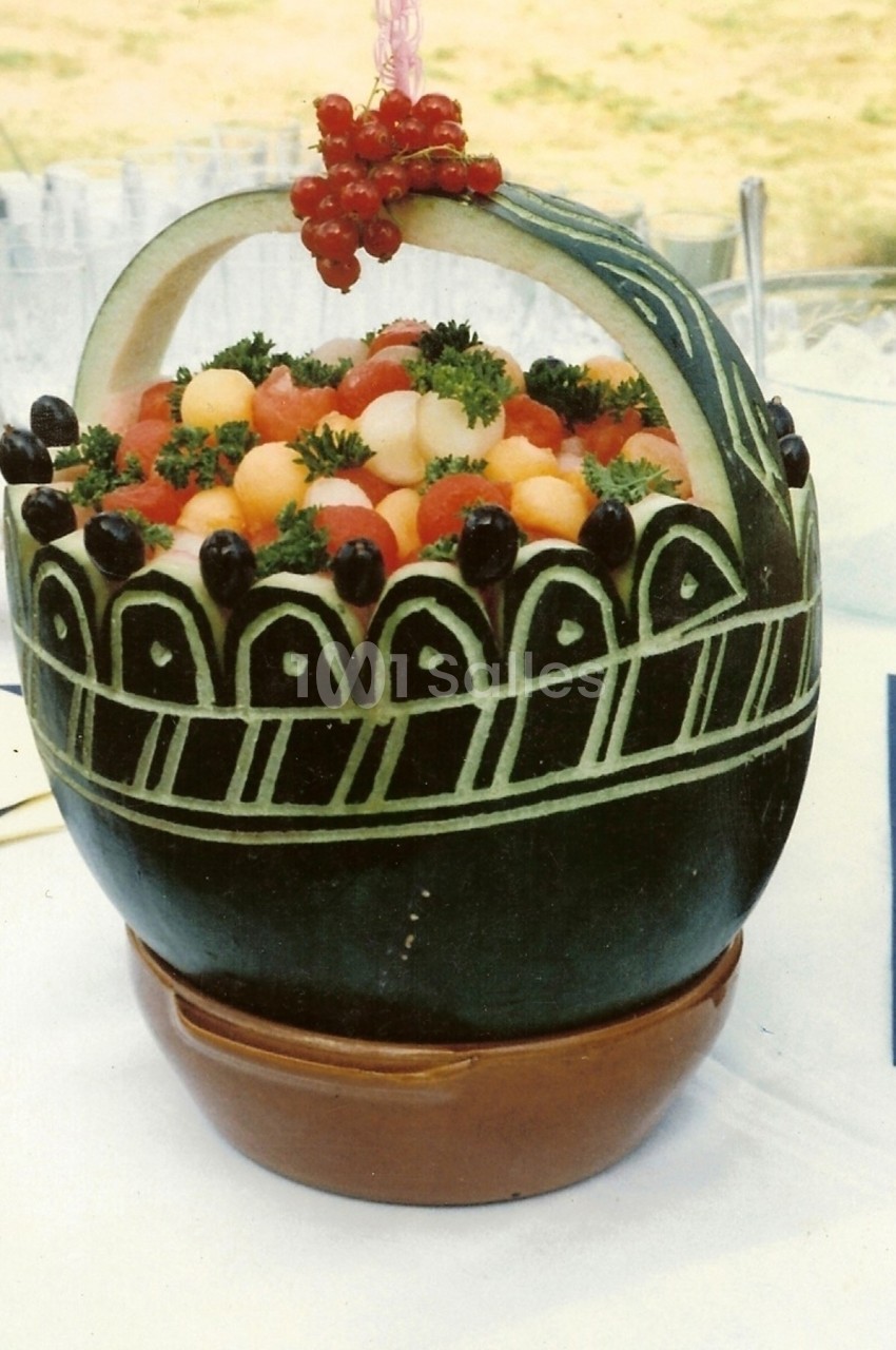 Panier sculpté dans une pastèque, rempli de billes de fruits colorés, décoré de groseilles et de persil.