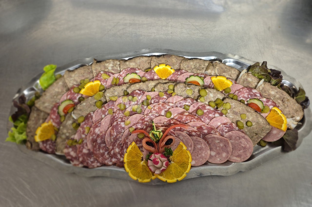 Plateau de charcuterie variée avec tranches de saucisson, pâté et décorations d'oranges, cornichons et salade.