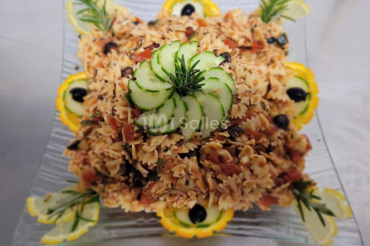 Assiette de pâtes farfalle garnie de légumes, olives noires, rondelles de concombre et décorations de citron.