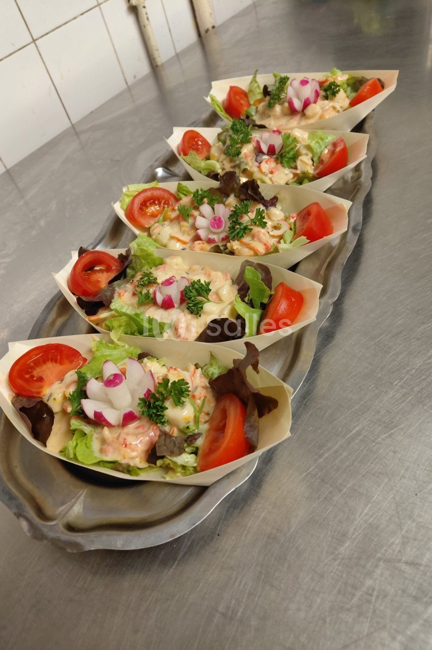 Plateau de petites barquettes garnies de crudités, tomates, radis et persil, disposé sur un plan de travail en inox.