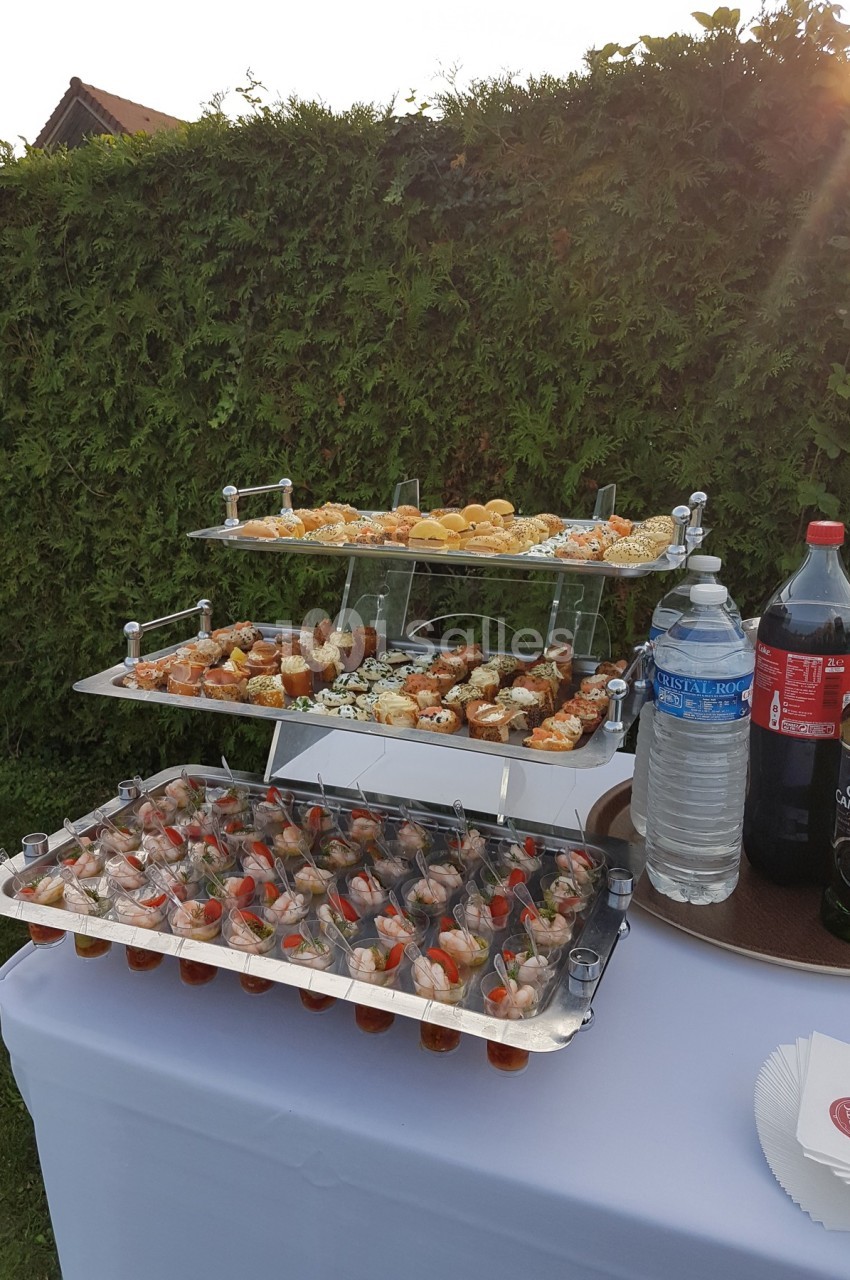 Plateau de verrines et amuse-bouches variés disposés sur une table en extérieur, avec des boissons à côté.