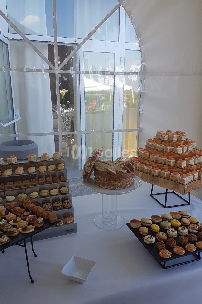 Buffet de petits fours salés et sucrés disposés sur des présentoirs dans une salle lumineuse avec vue sur l'extérieur.