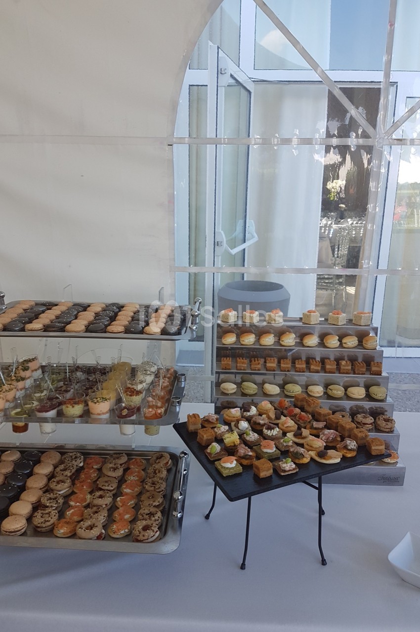 Buffet de petits fours variés disposés sur des plateaux dans un cadre lumineux avec une tente blanche en arrière-plan.