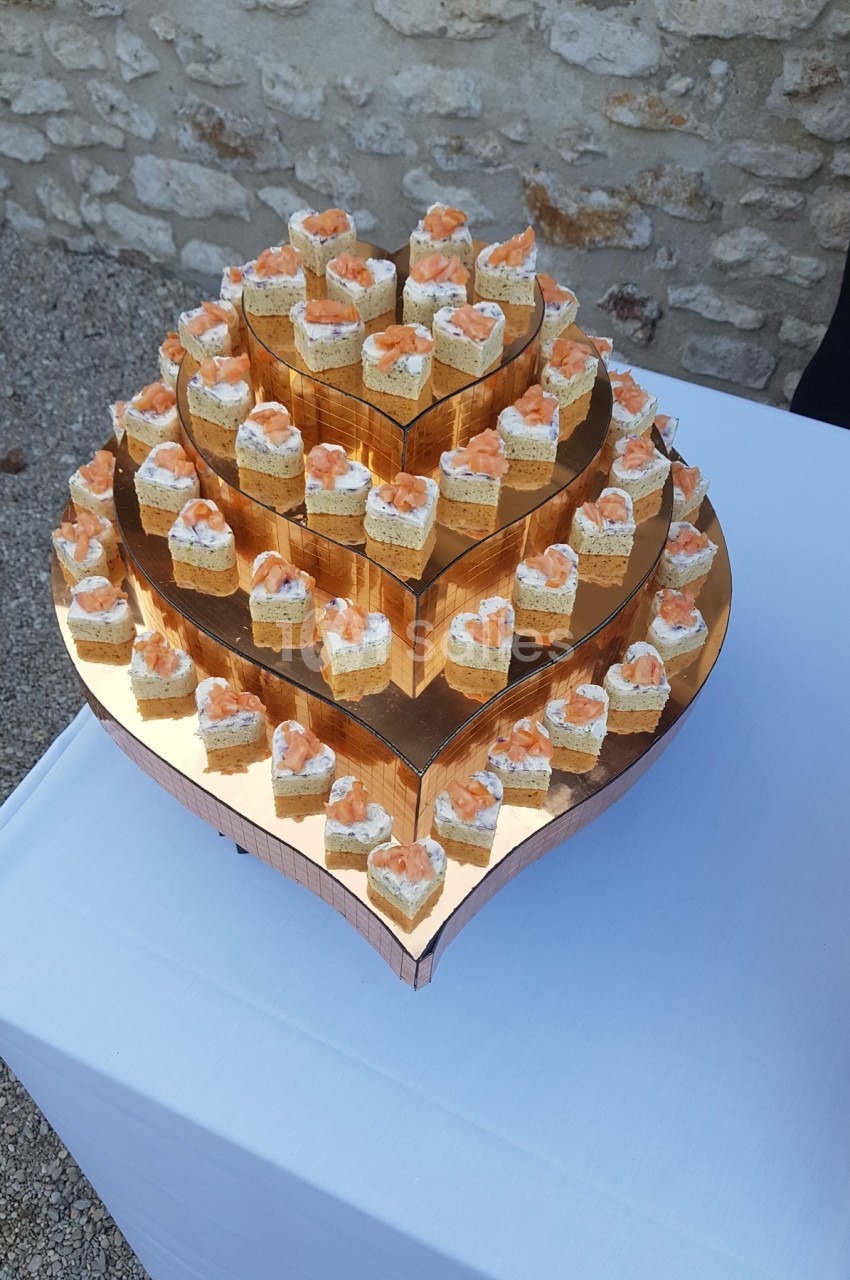Plateau en forme de cœur avec des bouchées apéritives au saumon et crème disposées sur plusieurs niveaux.