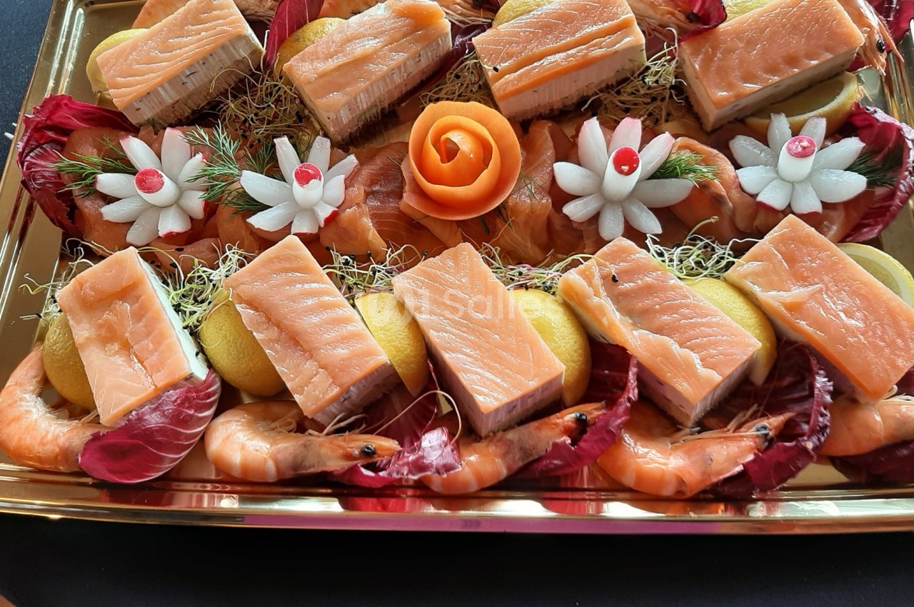 Plateau de saumon fumé, crevettes, radis sculptés et tranches de citron, décoré de salade et d'une rose en carotte.
