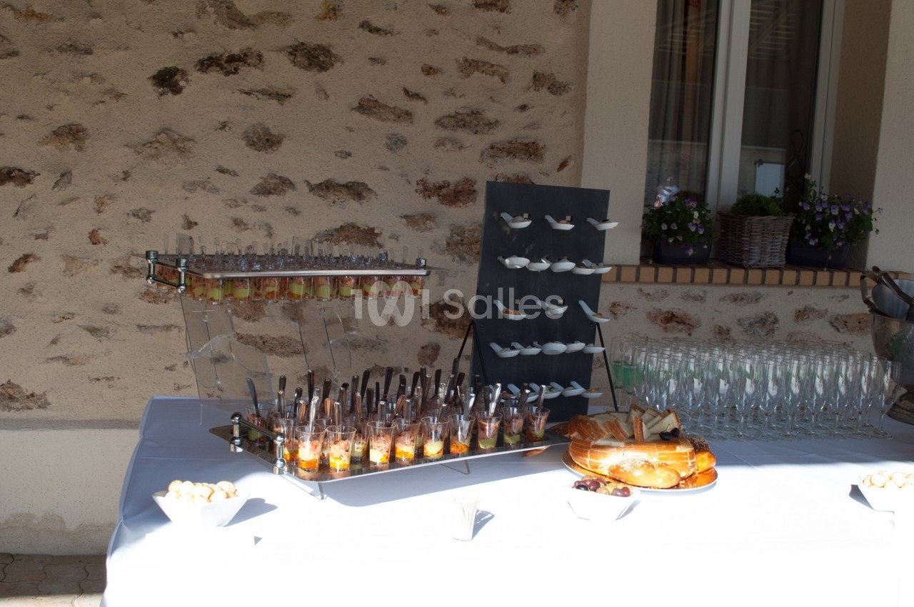 Table dressée en extérieur avec verrines, cuillères apéritives, pain, viennoiseries et verres à pied alignés.