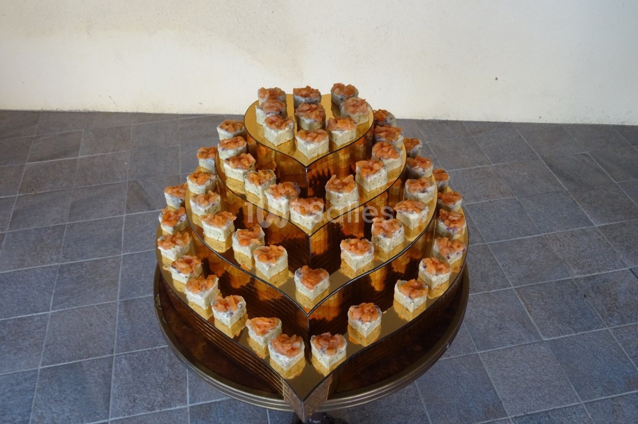 Présentoir en forme de cœur avec plusieurs étages de petits gâteaux individuels décorés, posé sur un sol carrelé.
