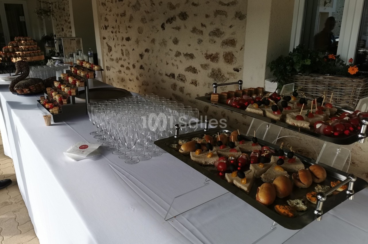 Buffet avec verrines, amuse-bouches, pains garnis et verres vides disposés sur une table blanche en extérieur.