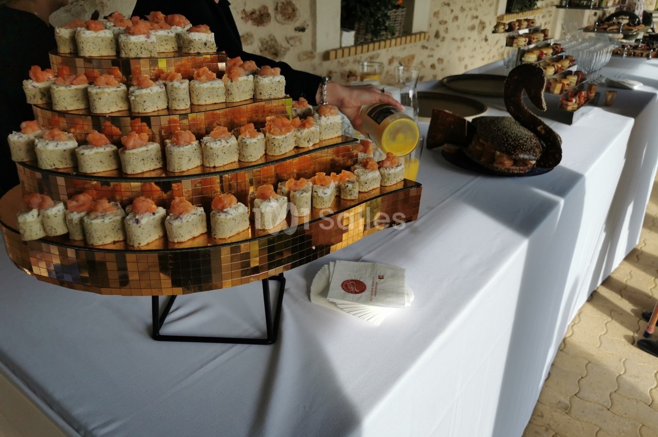 Plateau de verrines garnies de saumon et de crème disposé sur une table de buffet habillée d'une nappe blanche.