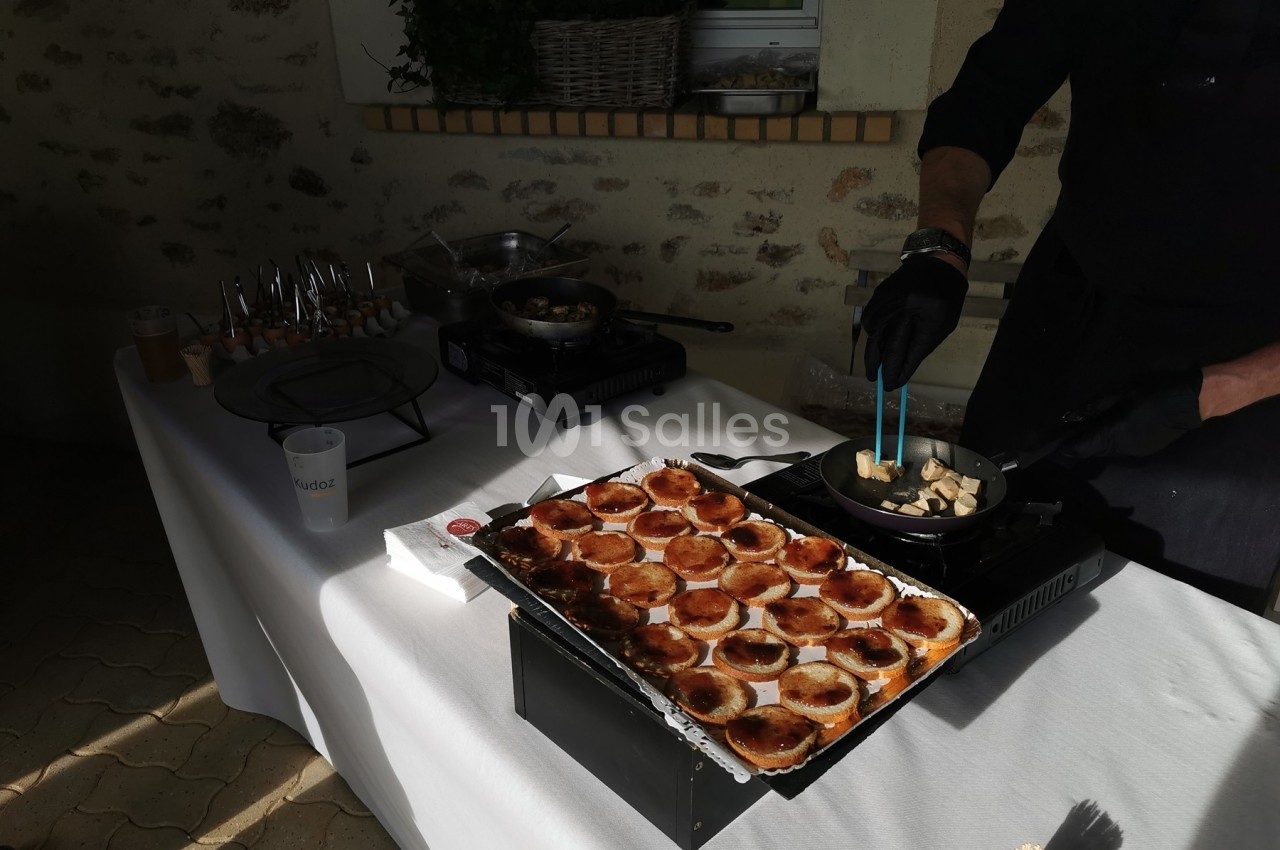 Un cuisinier prépare des aliments dans une poêle à côté d'une table garnie de bouchées apéritives.