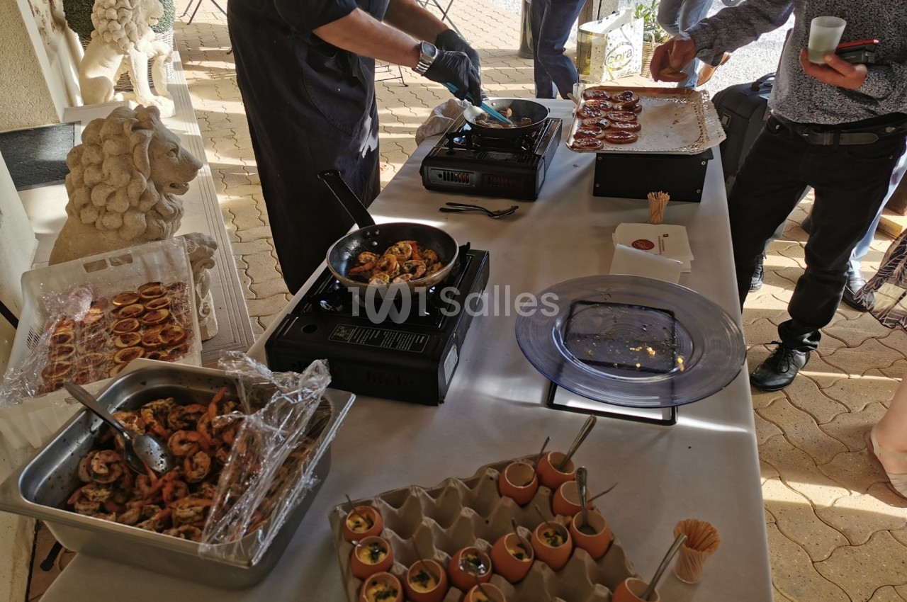 Chef cuisinant des plats à base de crevettes et œufs devant une table dressée en extérieur.