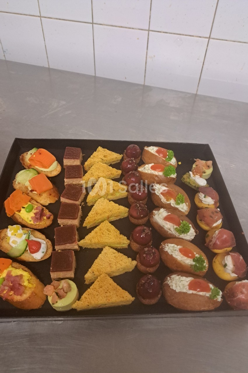 Plateau de canapés variés comprenant toasts, bouchées salées et amuse-bouches disposés sur une table en inox.
