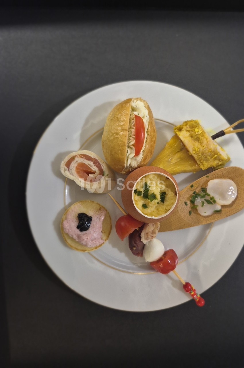 Assortiment de bouchées apéritives variées disposées sur une assiette blanche, présenté sur une table noire.