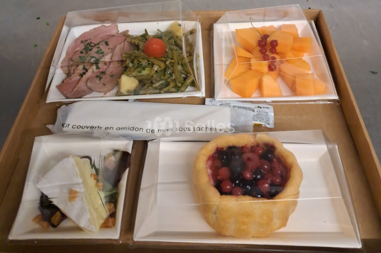 Plateau-repas composé de viande, légumes, fromage, dessert aux fruits rouges et salade de melon, avec couverts inclus.