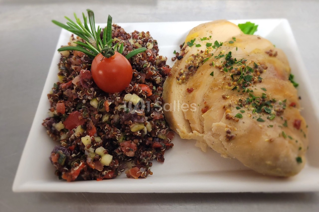 Assiette avec filet de poulet tranché, accompagné de quinoa aux légumes et décoré d'une tomate cerise et d'herbes.