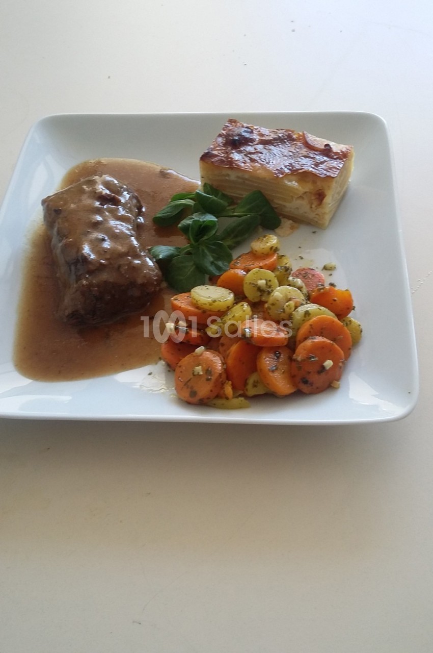 Assiette contenant un rôti en sauce, un gratin dauphinois et des légumes sautés, présentée sur une table blanche.
