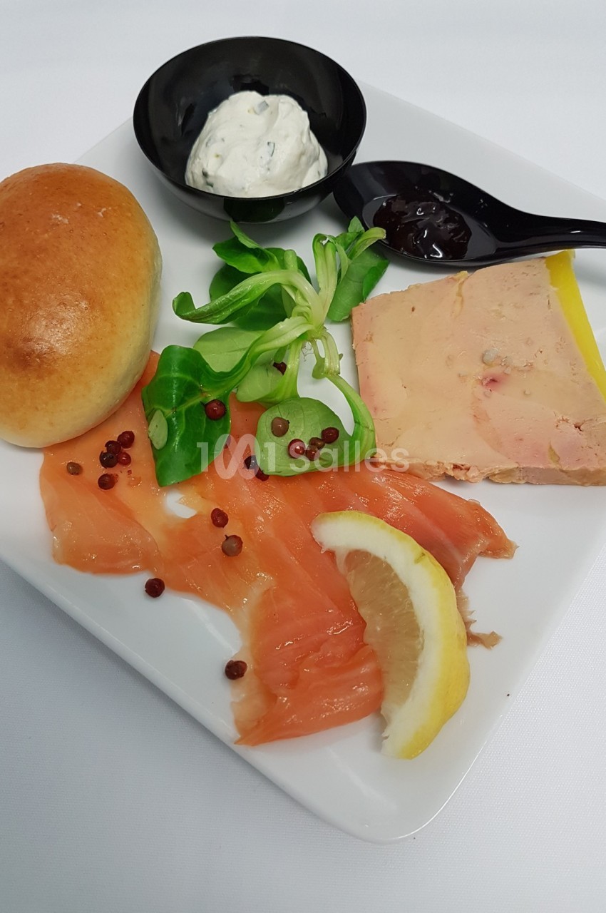Assiette composée de saumon fumé, foie gras, pain brioché, salade, crème et confiture sur un fond blanc.