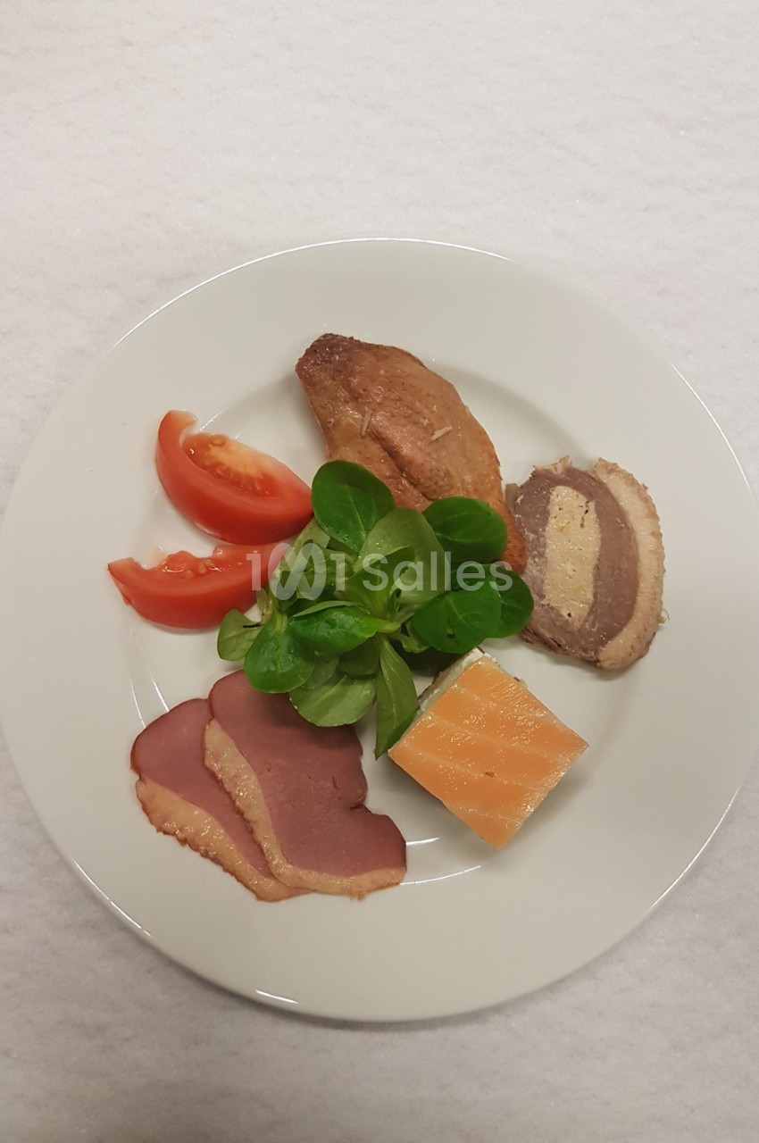 Assiette contenant du magret de canard fumé, du foie gras, de la salade mâche, des tranches de tomate et un morceau de…