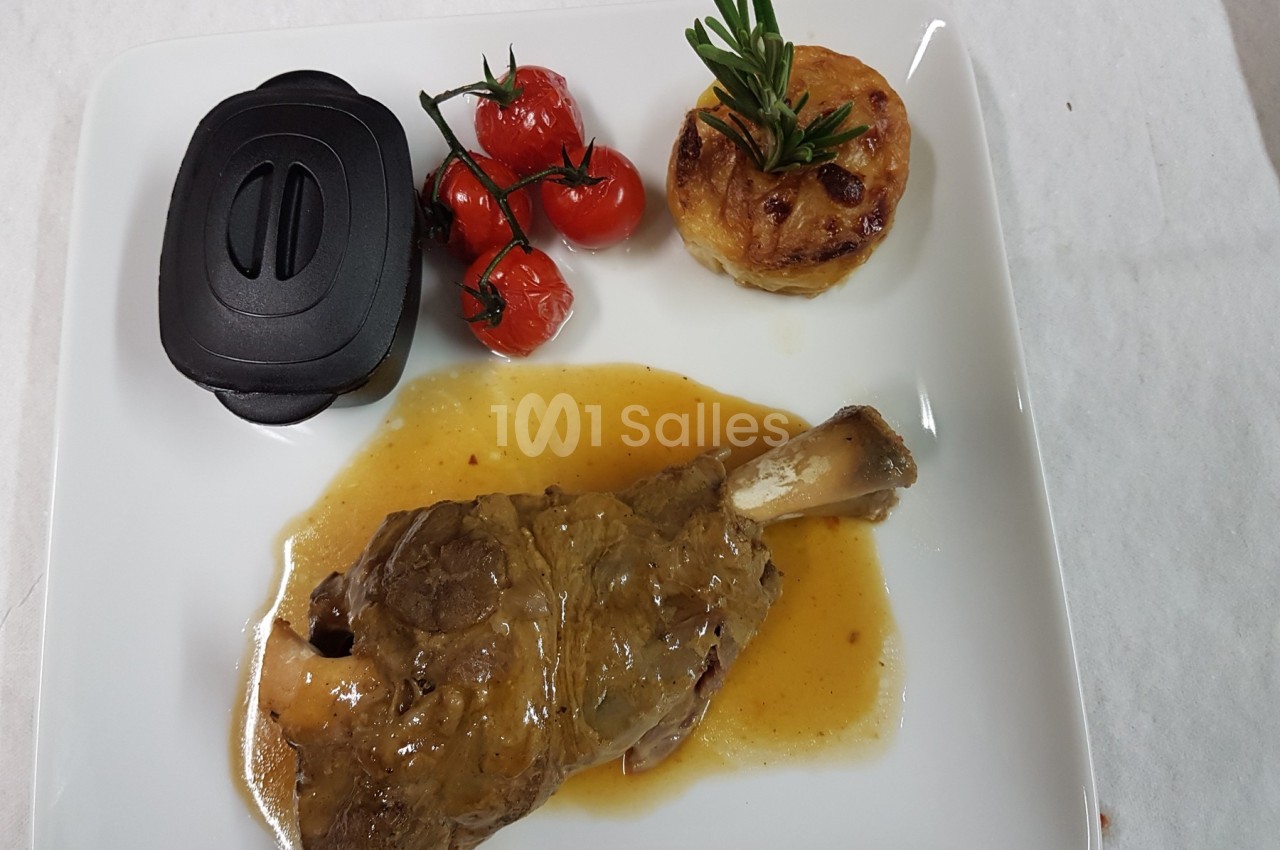 Assiette contenant un jarret d'agneau en sauce, une garniture de pommes de terre gratinées et des tomates cerises rôties.