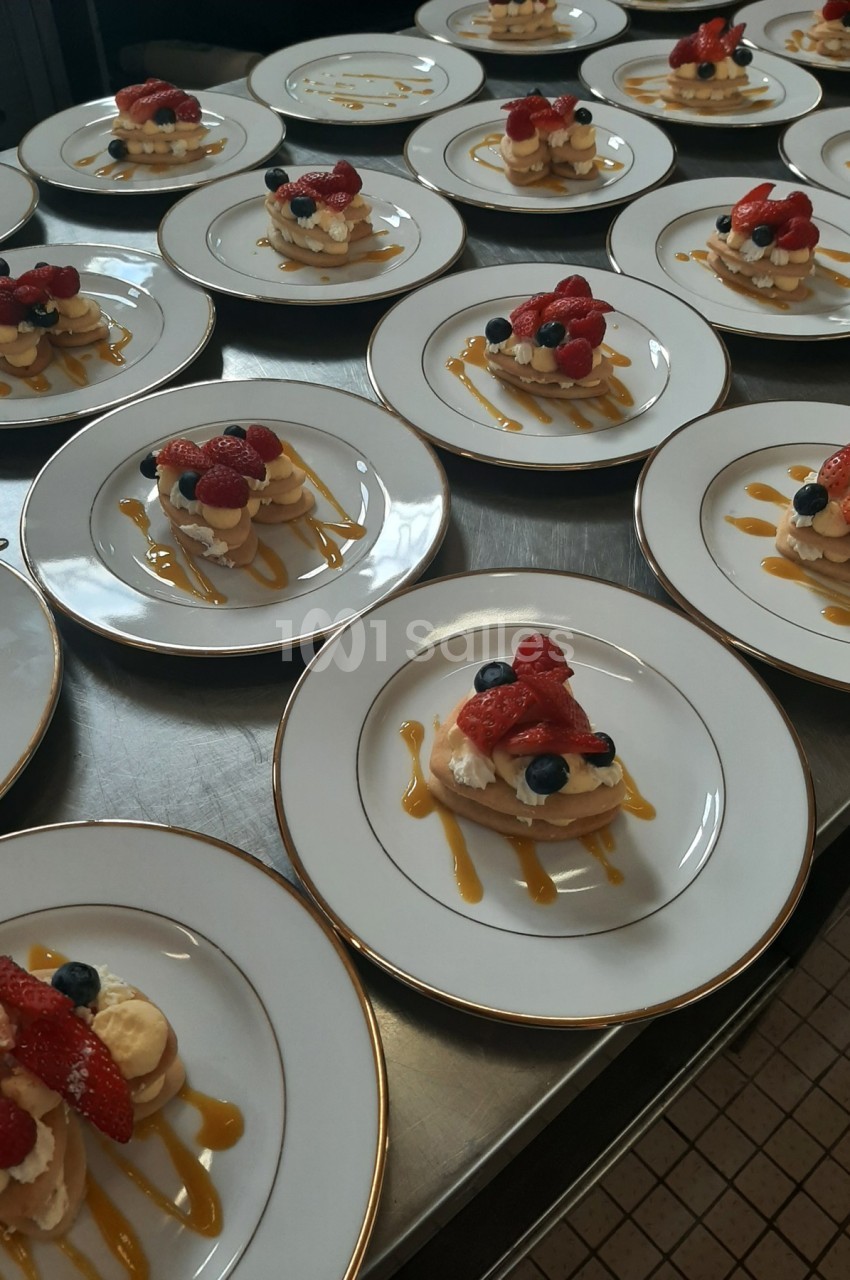 Assiettes de desserts individuels composés de fruits rouges, crème et caramel, disposées sur une table en cuisine.