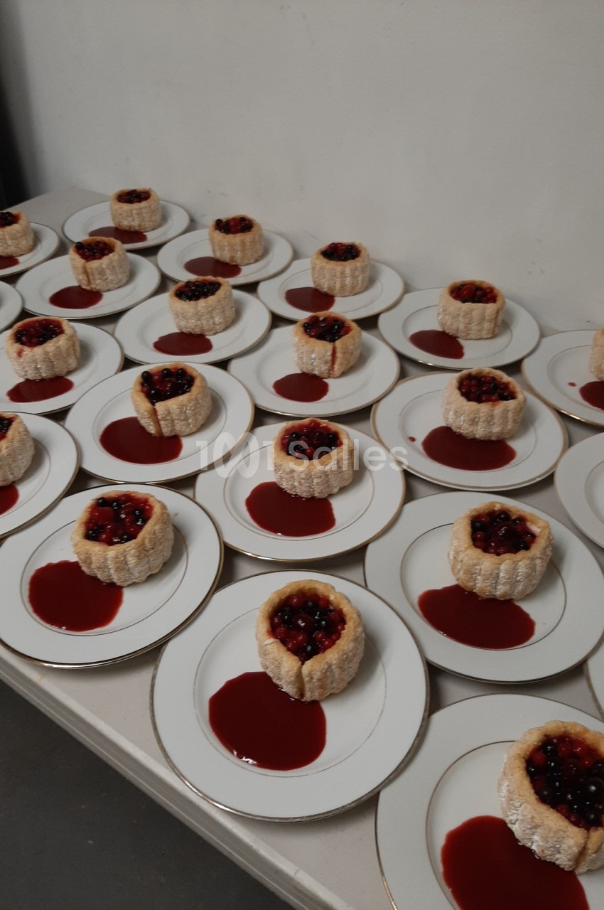 Assiettes alignées contenant des charlottes individuelles garnies de fruits rouges et entourées de coulis.