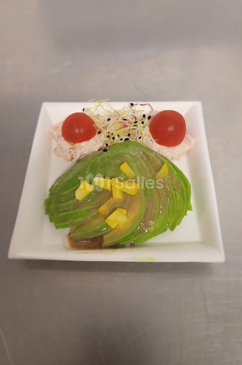 Tranches d'avocat disposées en éventail avec tomates cerises, germes et dés de poivron dans une assiette carrée blanche.