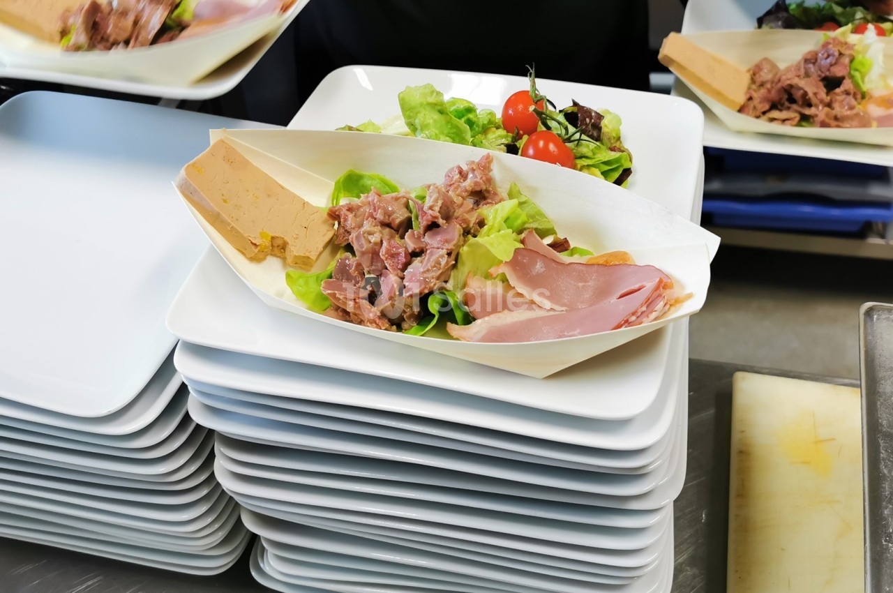 Assiette contenant de la salade, des tomates cerises, du pâté, du jambon et de la viande froide, posée sur une pile d…