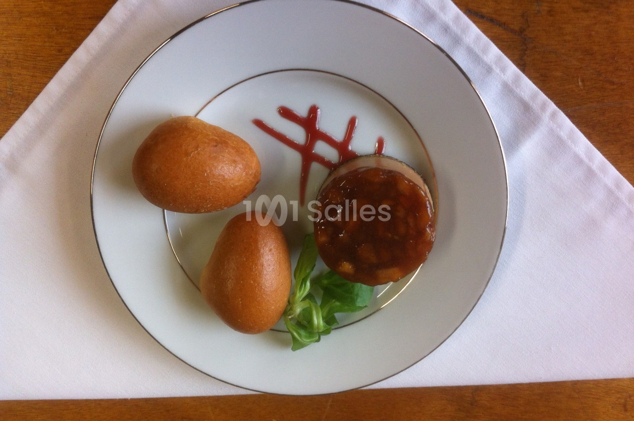 Assiette contenant deux petits pains, un médaillon de viande nappé de sauce, une feuille de salade et un trait de sauce…