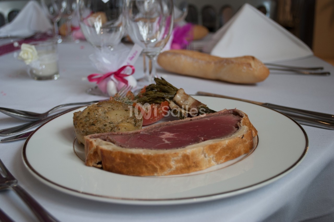 Assiette de bœuf en croûte accompagné de légumes, servie sur une table dressée avec couverts et verres.
