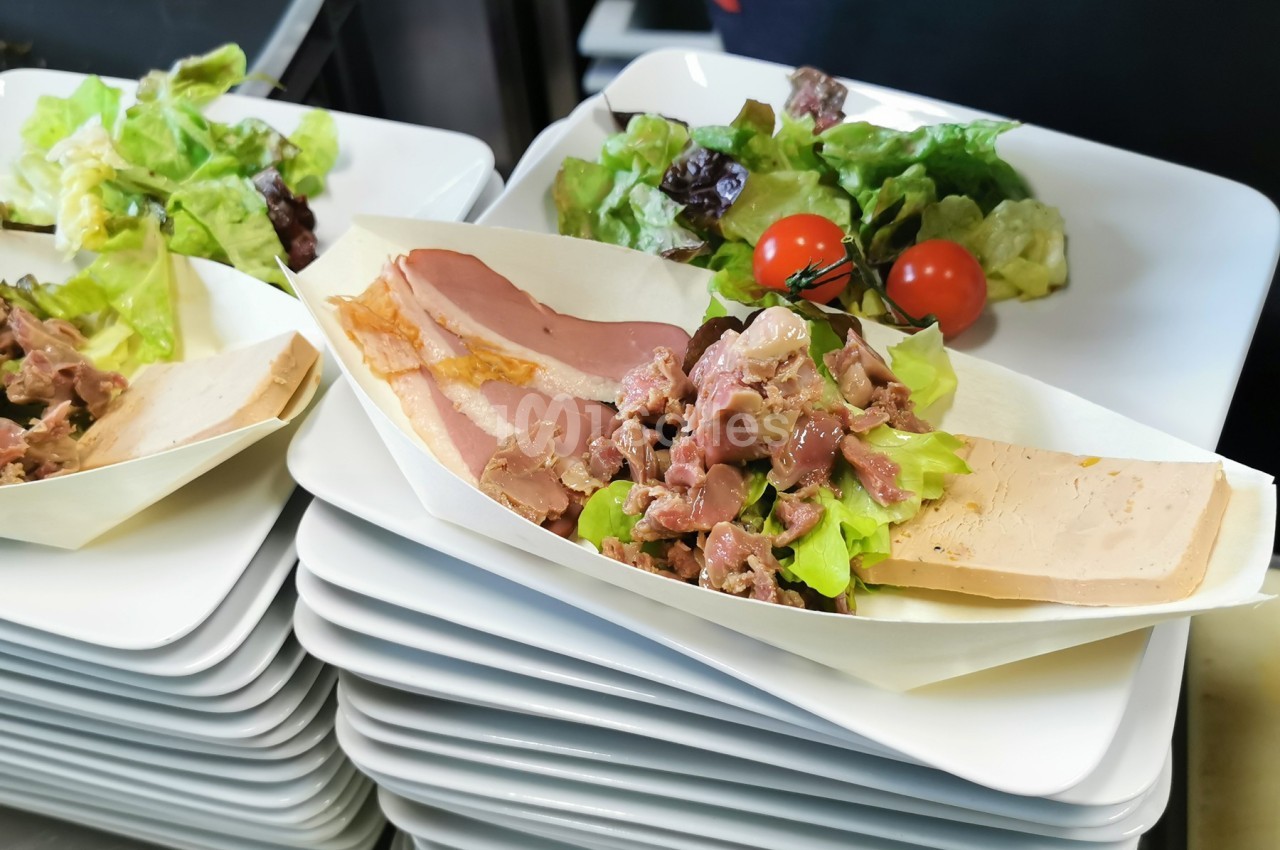 Assiette de charcuterie avec foie gras, salade verte, tomates cerises et viande froide, présentée sur des assiettes empilées.