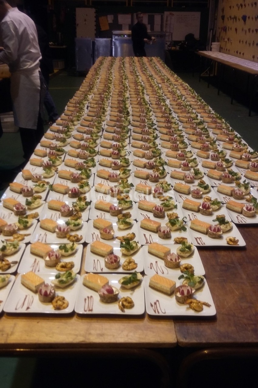 Des dizaines d'assiettes identiques alignées sur une longue table, contenant des desserts et des garnitures.