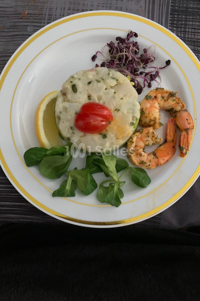 Assiette composée d'un tartare de poisson, crevettes marinées, mâche, germes de radis et tranche de citron.