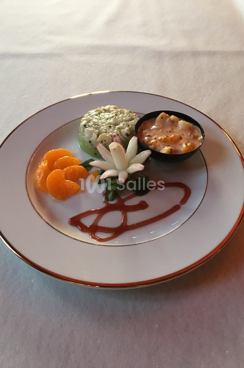 Assiette contenant un tartare, des quartiers de mandarine, une décoration florale et une sauce en ramequin.