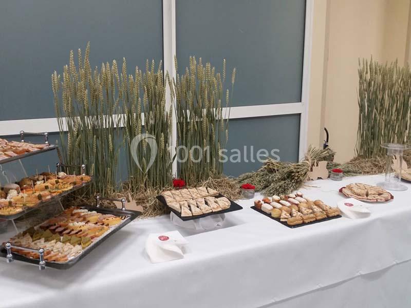 Buffet de pâtisseries et amuse-bouches disposé sur une table blanche, décorée avec des épis de blé en arrière-plan.