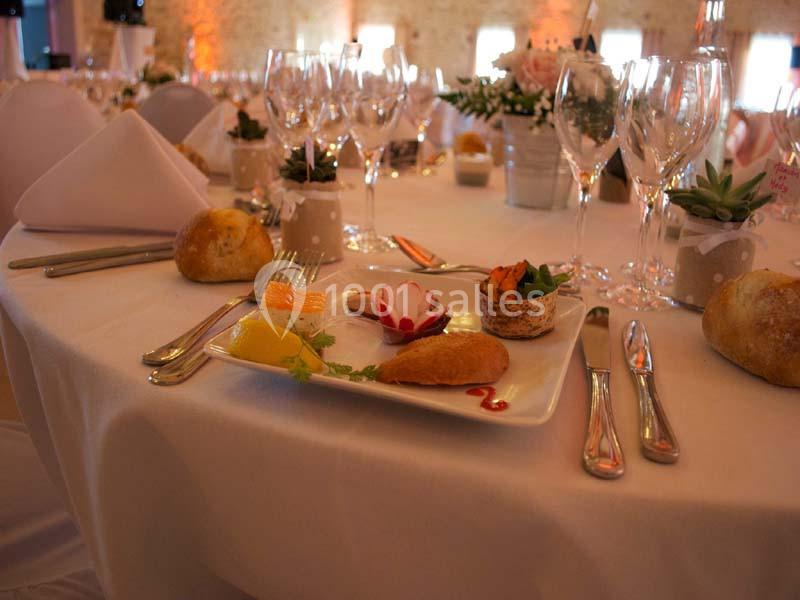 Table dressée avec assiette de mise en bouche, couverts, verres à pied et décoration florale dans une salle éclairée.