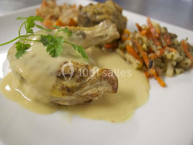 Assiette de volaille nappée de sauce, accompagnée de légumes sautés et d'une garniture en arrière-plan.
