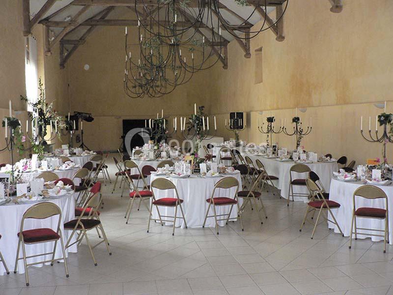 Salle de réception décorée avec des tables rondes, nappes blanches, chaises pliantes et chandeliers noirs.