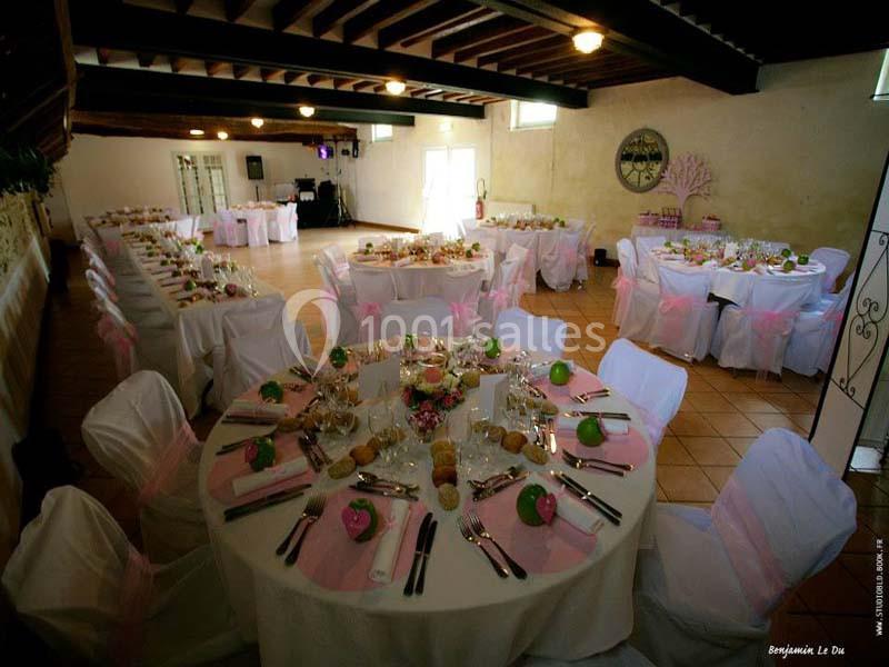 Salle de réception décorée avec des tables rondes dressées, nappes blanches et accents roses, sous un plafond en bois.