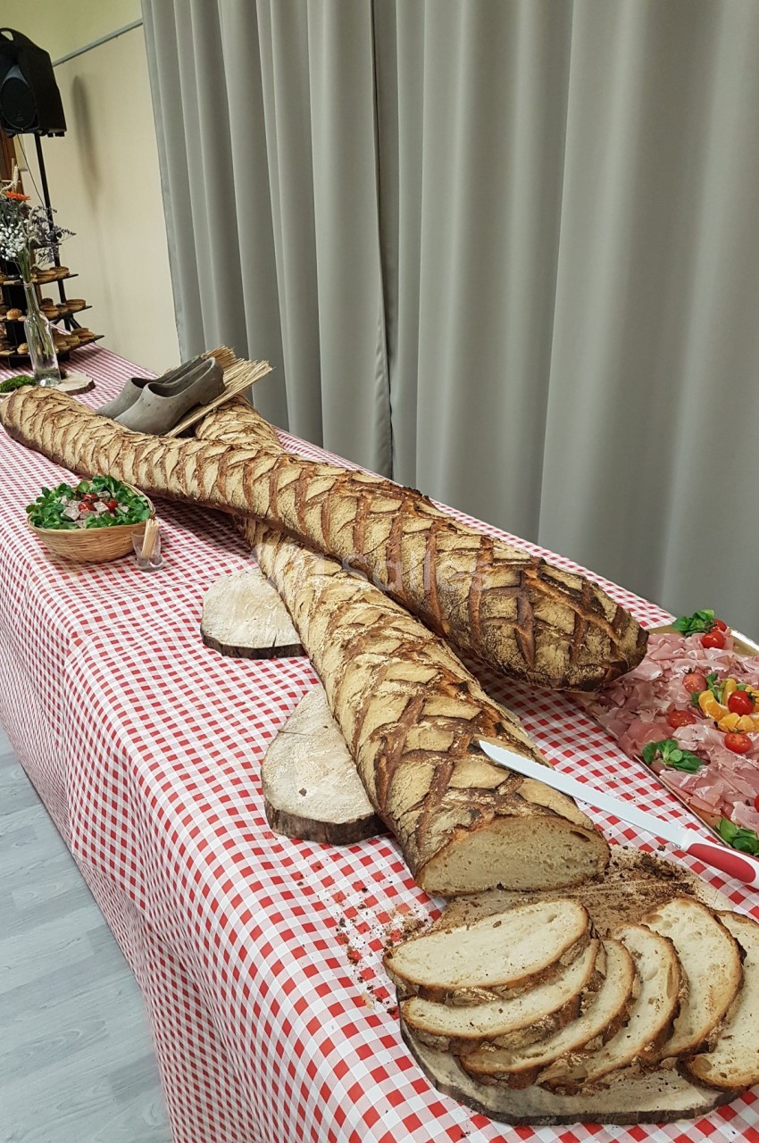Deux longues baguettes de pain artisanal posées sur une nappe à carreaux rouges, entourées de charcuterie et de garnitures.