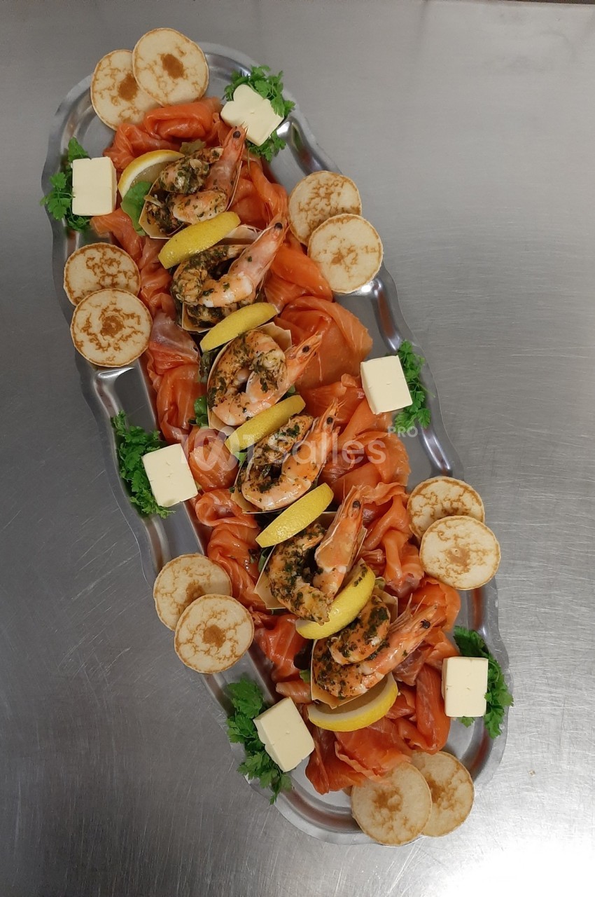 Plateau de fruits de mer avec crevettes, saumon fumé, rondelles de citron, blinis, beurre et garniture verte.