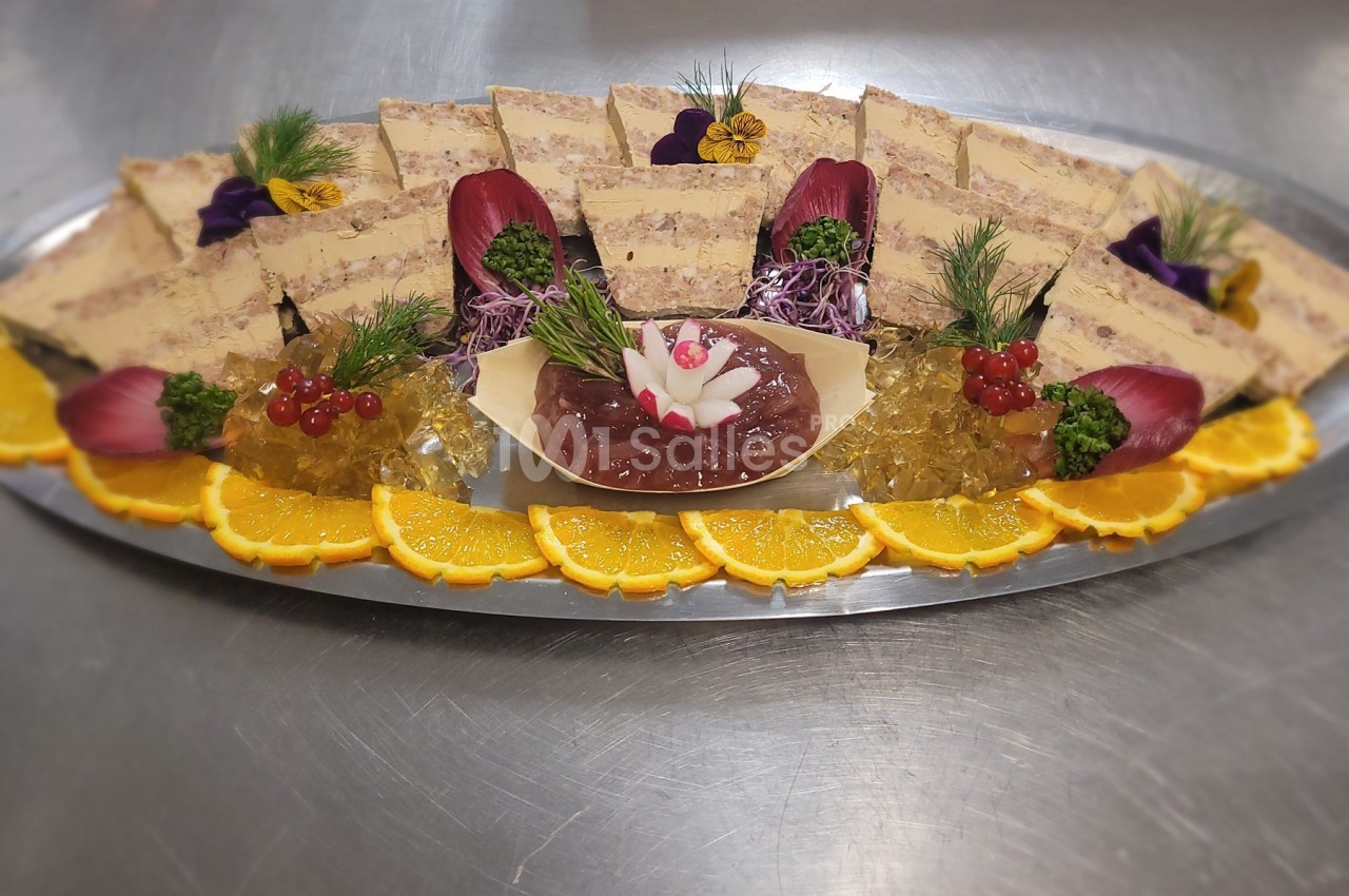 Plateau de terrines garnies de gelée, tranches d'orange, groseilles et décorations florales sur une table en inox.