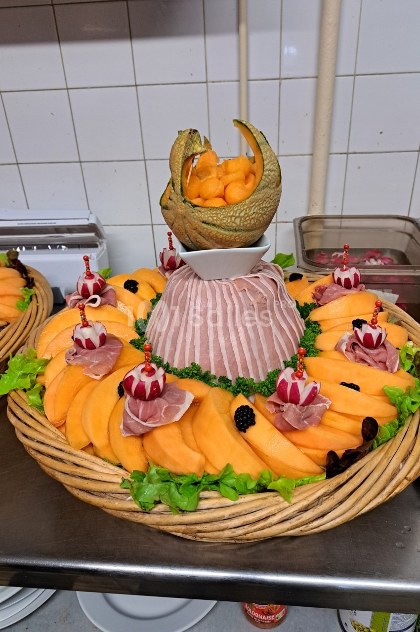 Plateau de présentation avec tranches de melon, jambon cru, décorations de radis et boulettes de melon dans une coque.